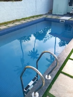 Una piscina con agua azul cristalina, barandillas metálicas y borde de azulejos.