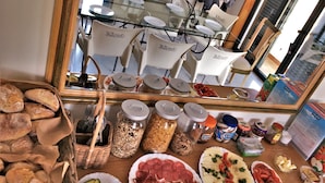 A breakfast buffet with various food items, including bread, cheese, and meats, arranged on a table. - Slide Surfcamp (Vagos)