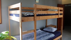 A bunk bed with a wooden frame, a lower bed with a patterned blanket, and a pillow. - Slide Surfcamp (Vagos)