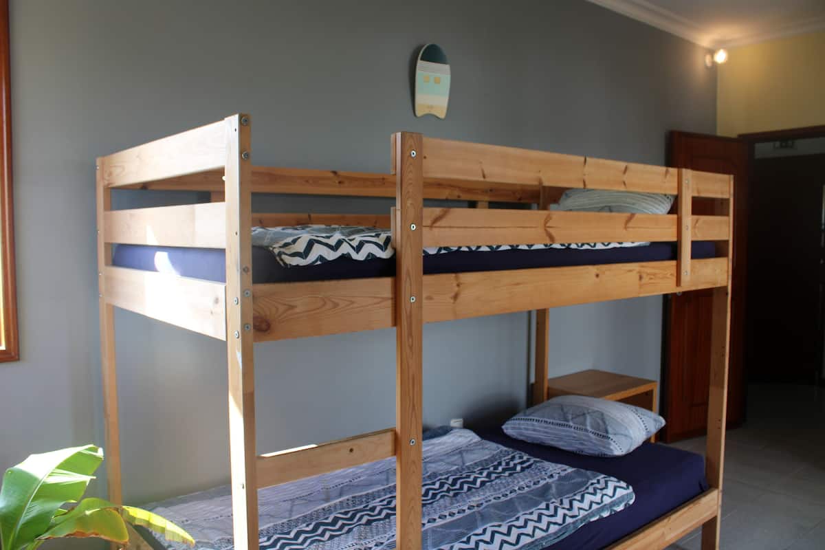 Ein Etagenbett mit Holzrahmen, ein Bett unten mit gemustertem Bettbezug und einem Kopfkissen.