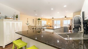 A modern kitchen with a granite countertop, white cabinetry, and a dining area with chairs. - Ambassador Villas 401 Oceanfront 7 Br 6 Ba (North Myrtle Beach)