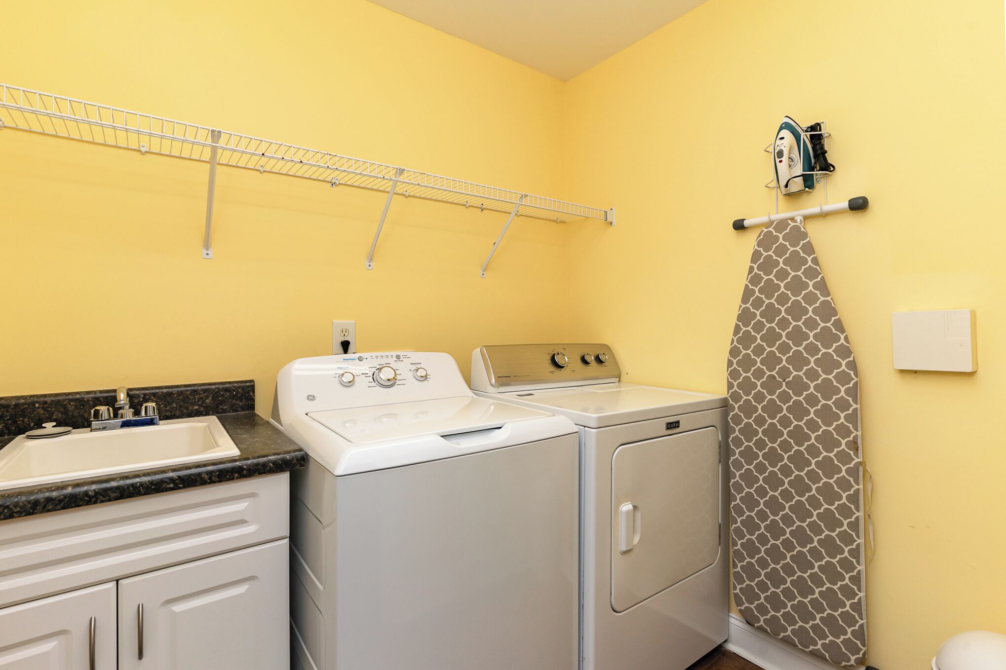 A laundry room with a washing machine, dryer, and ironing board.