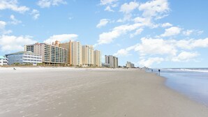 A wide sandy beach with high-rise buildings in the background. - Ambassador Villas 401 Oceanfront 7 Br 6 Ba (North Myrtle Beach)