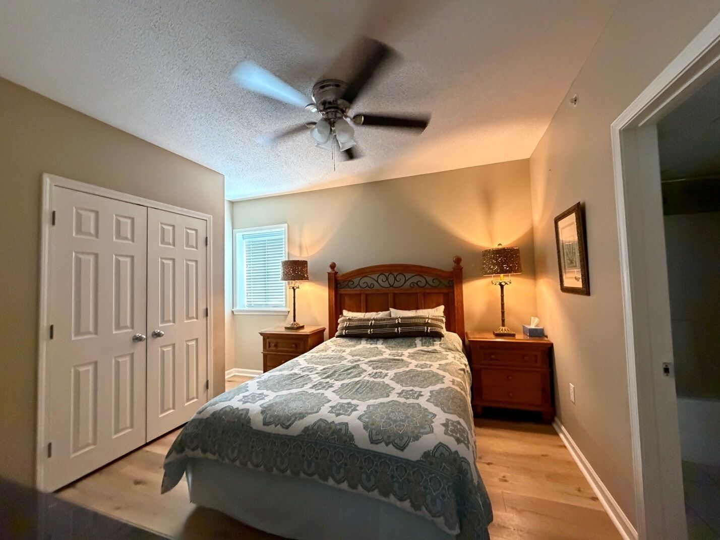 A bedroom with a bed, two bedside tables with lamps, a ceiling fan, a door, and a window.