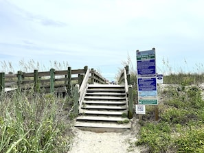 En trætrap ned til en strand med et skilt, der viser strandens regler, og en QR-kode for yderligere information.