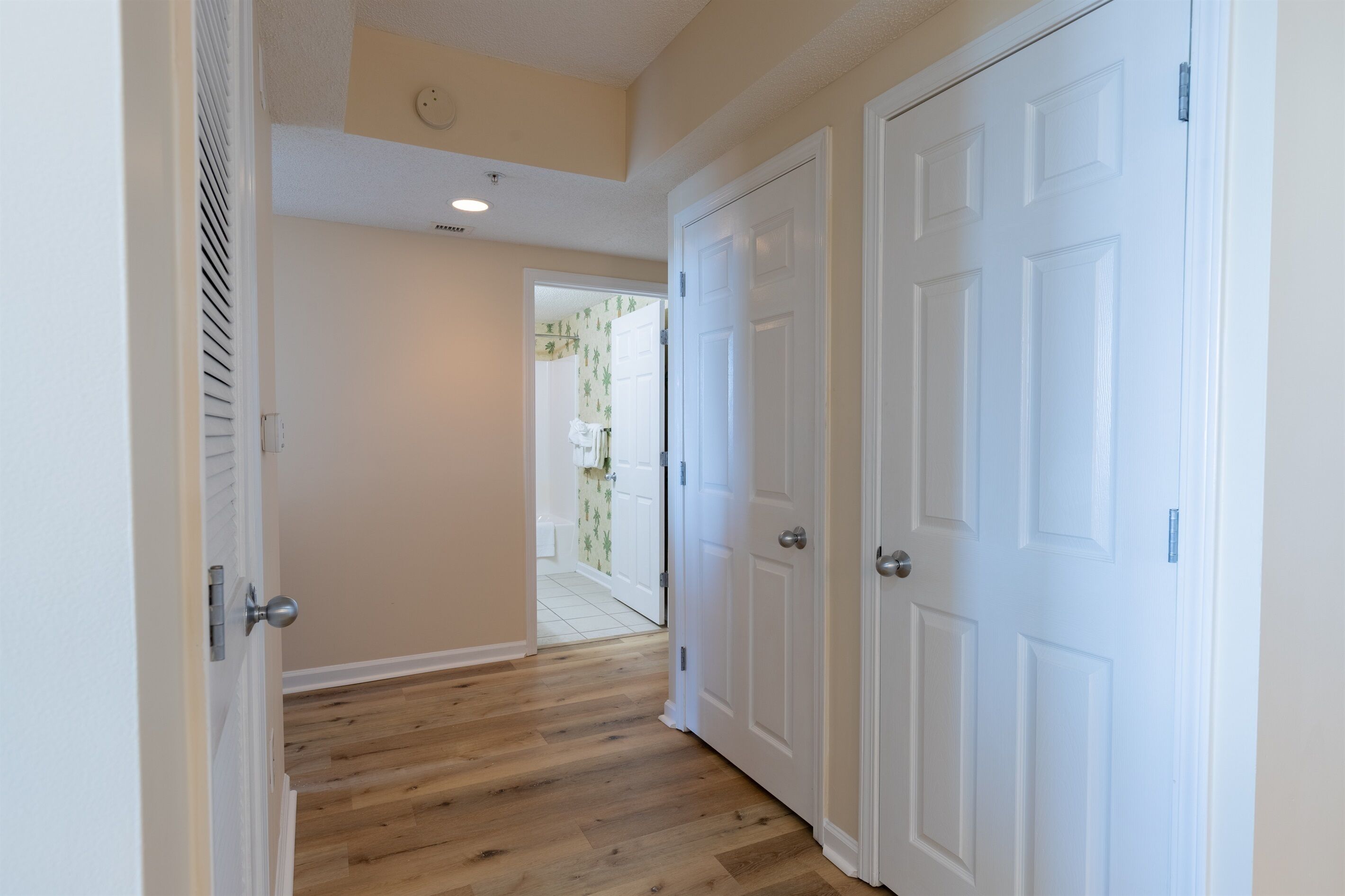 A hallway with wooden flooring, white walls, and two white doors.