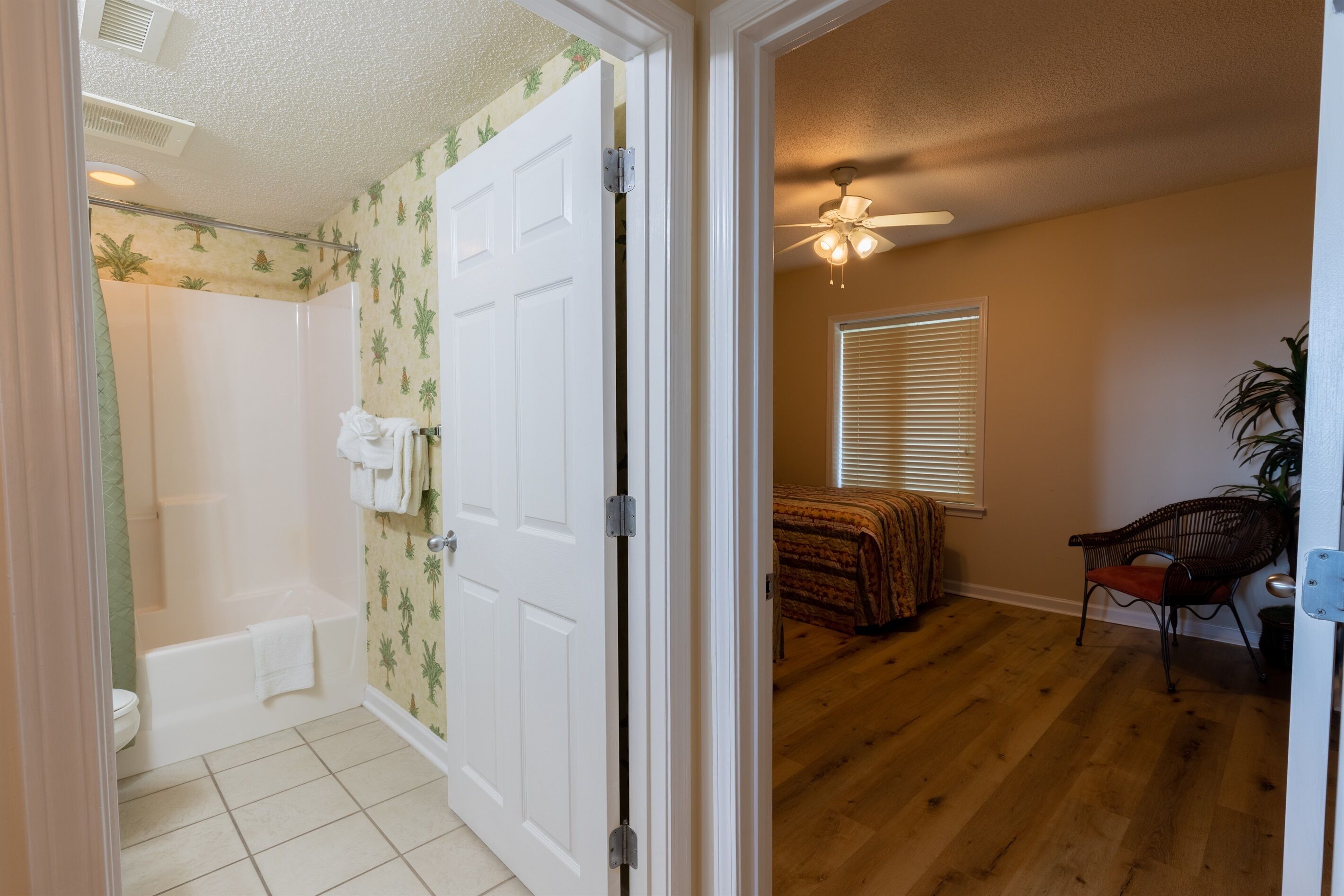 A bathroom with a bathtub and toilet, a bedroom with a bed and window, and a chair in a living area.