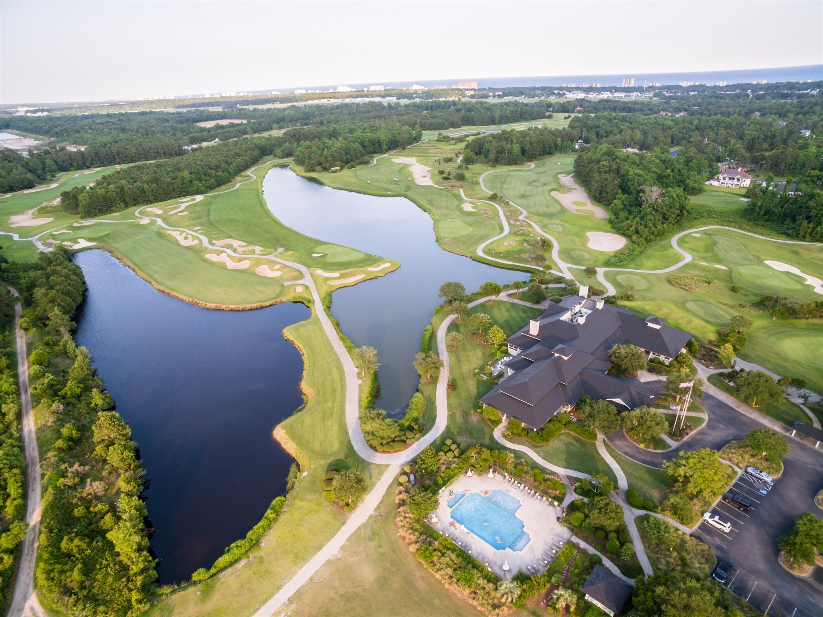 An aerial view of a golf course with a large lake, a swimming pool, and a clubhouse.