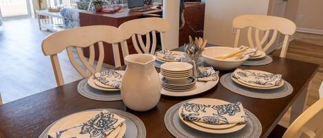 Una mesa de comedor dispuesta con platos azules y blancos, una jarrón blanco y cuencos apilados.