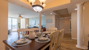 A dining area with a wooden table set for four, white chairs, and a chandelier. - Barefoot N Tower 404- Golf, Pool, Free Shuttle (North Myrtle Beach)