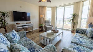 A spacious living room with a ceiling fan, a flat-screen TV, a sofa set, a coffee table, and a balcony with a view. - Barefoot N Tower 404- Golf, Pool, Free Shuttle (North Myrtle Beach)