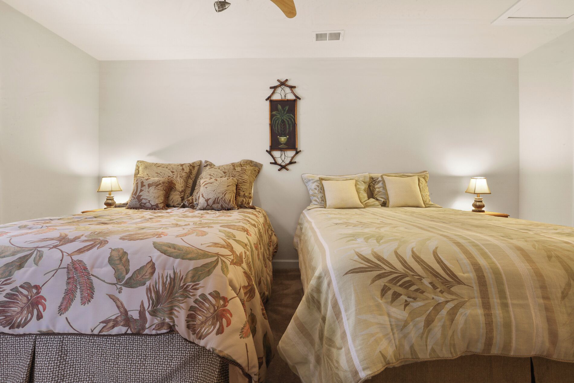 A bedroom with two beds, each with floral-patterned bedding, a wall-mounted light fixture, and a ceiling fan.
