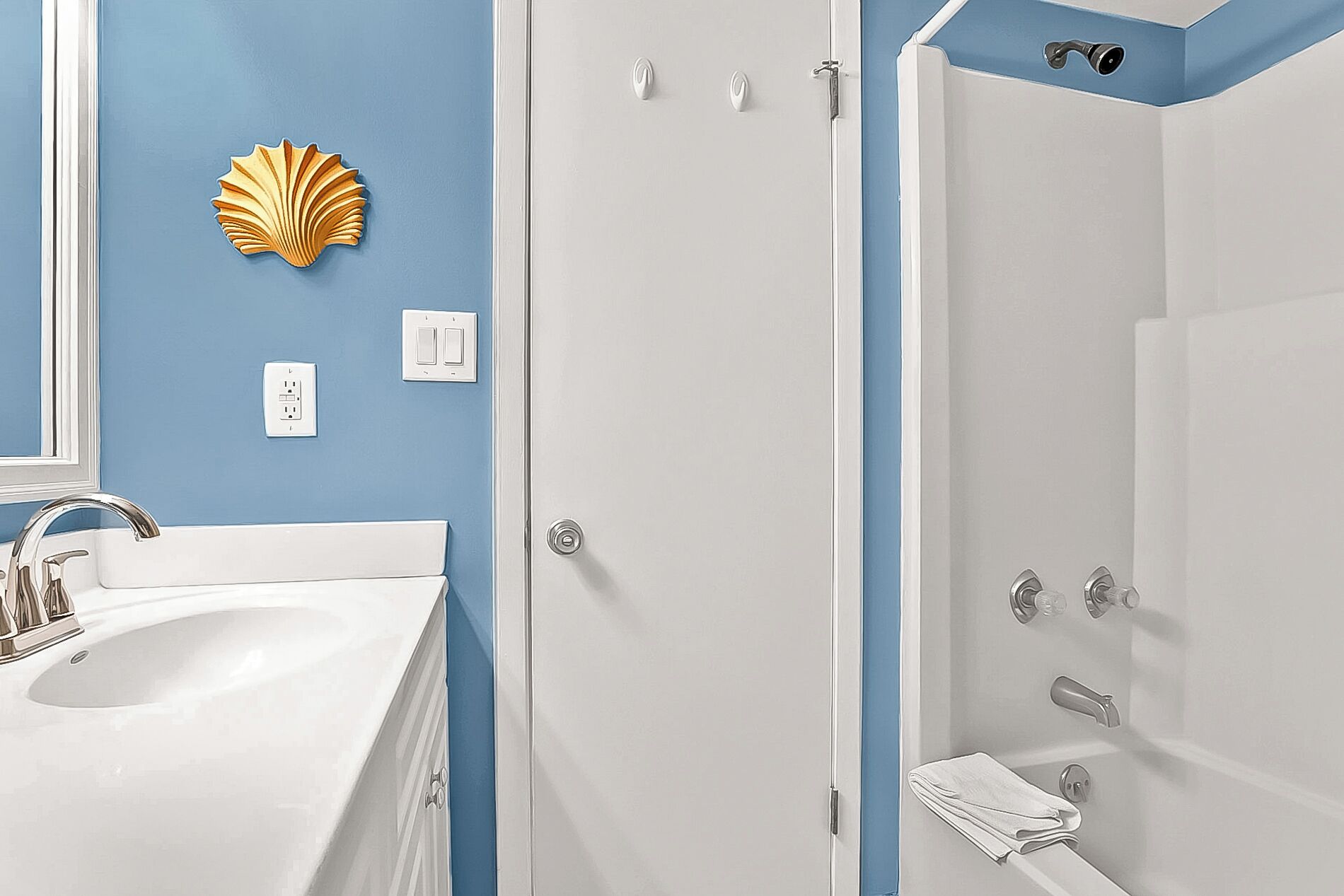Een badkamer met een witte wasbak, een spiegel, een blauwe wand, een witte deur en een douchegedeelte.