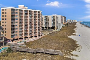 A beachfront hotel with multiple floors, balconies, and a beach access walkway.