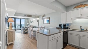 Een keuken met witte kastjes, een centraal eiland en een eethoek met stoelen.