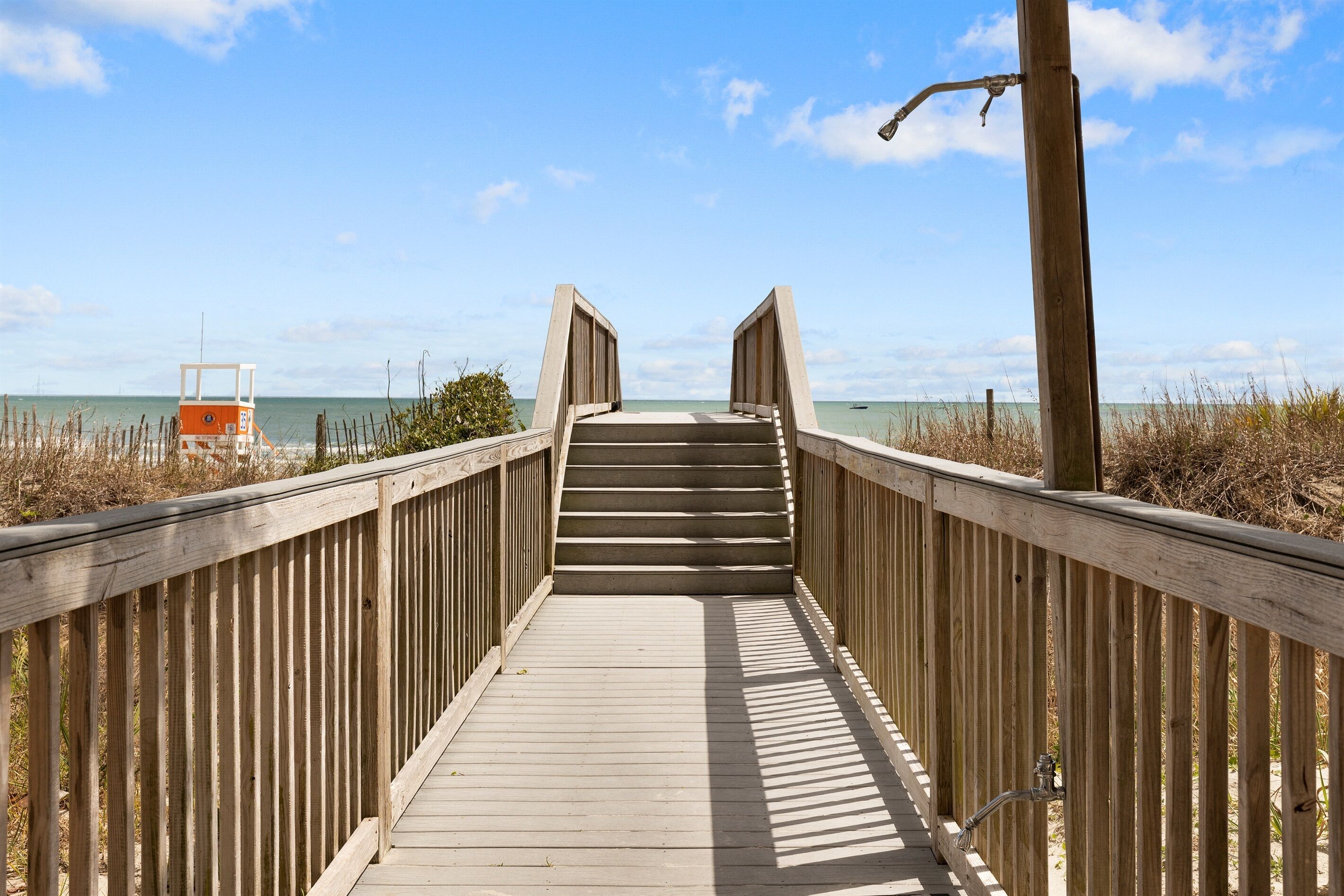 Une promenade en bois menant à une plage où se trouve un poste de surveillance des sauveteurs.