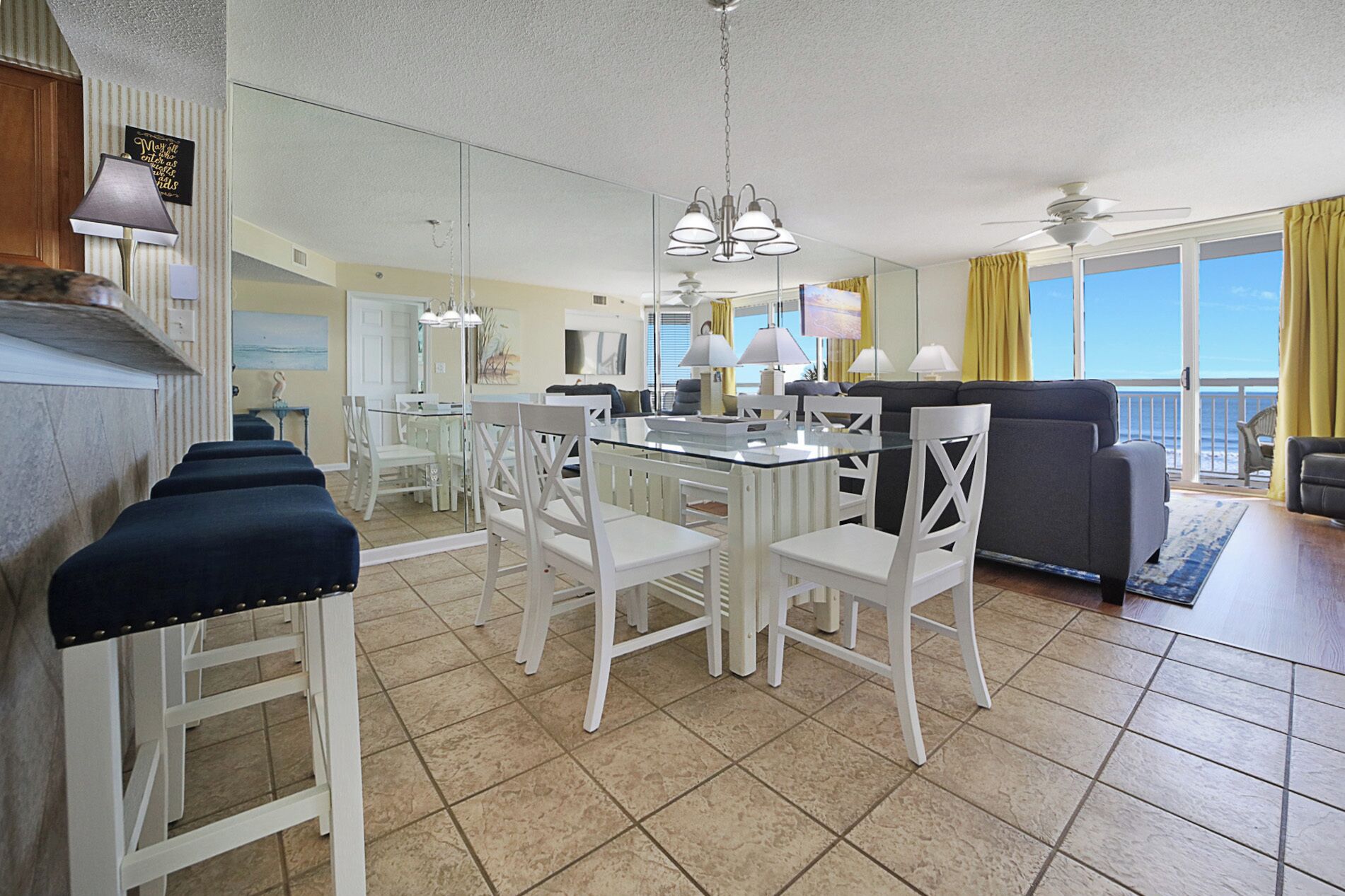 A spacious living area with a dining table, white chairs, a sofa, and a balcony with a view.