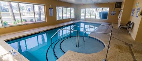 An indoor swimming pool with clear water, a tiled floor, and a pool ladder.