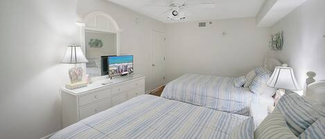 Une chambre avec deux lits, un ventilateur de plafond, un téléviseur posé sur une commode et un miroir.