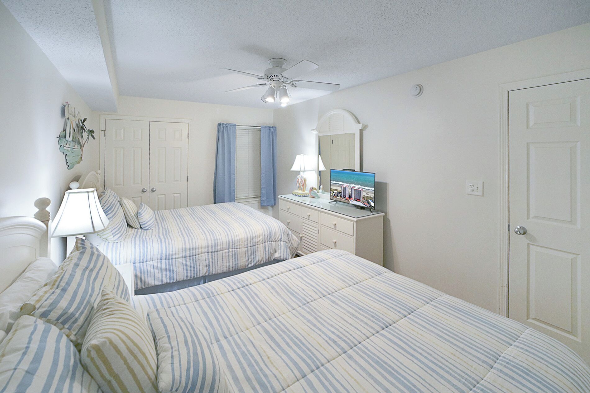 Une chambre avec deux lits, une commode, un ventilateur de plafond et un grand miroir.