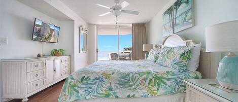 Quarto com cama, ventilador de teto, mesa de cabeceira, cômoda, televisão e vista para o exterior.