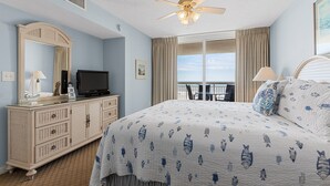 A bedroom with a bed, dresser, television, and a balcony with curtains.