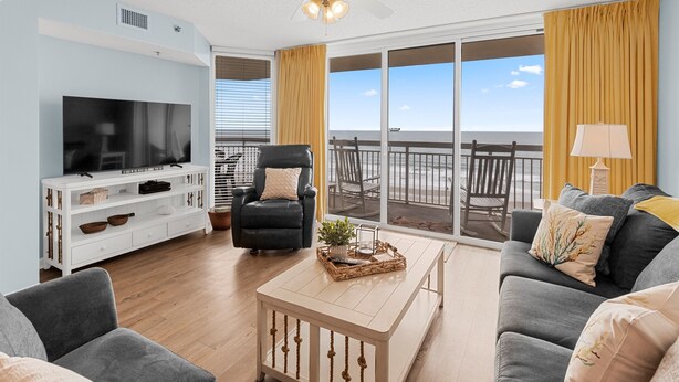 Una sala de estar con televisor, sofá, sillón y un balcón con vistas.