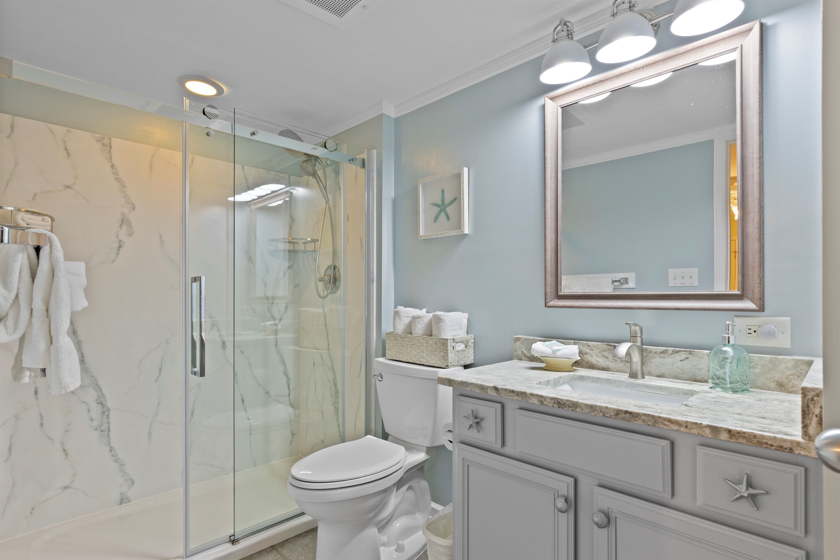 A modern bathroom with a glass-enclosed shower, a white toilet, and a vanity with a large mirror.