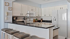 Una cocina moderna con armarios blancos, una isla central con taburetes de bar, un refrigerador de acero inoxidable y un microondas.