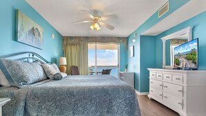 A bedroom with a bed, a dresser, a ceiling fan, and a window with a cityscape view. - Crescent Shores 807 Oceanfront, Pools, Lazy River (North Myrtle Beach)