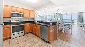 A modern kitchen with stainless steel appliances, wooden cabinets, and a large island with seating. - Crescent Shores 810 Oceanfront, Pools, Lazy River (North Myrtle Beach)