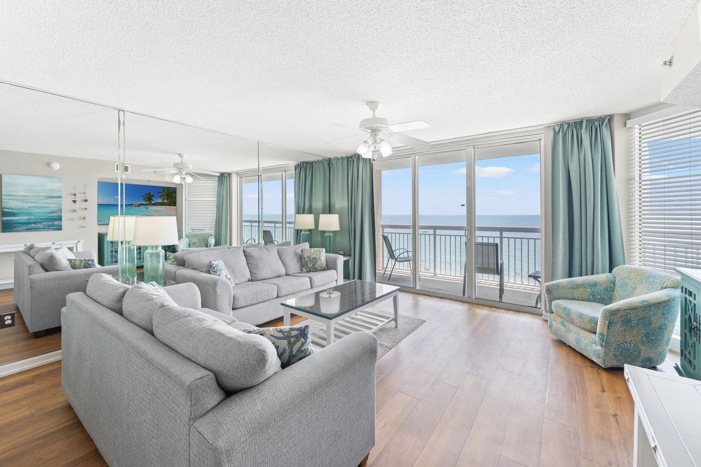 Un vaste salon avec balcon donnant sur la mer, aménagé avec des canapés gris et une table basse en verre.