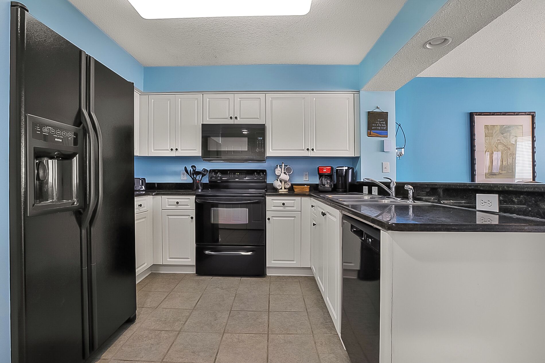 A compact kitchen with white cabinets, a black refrigerator, a microwave, and a stove.