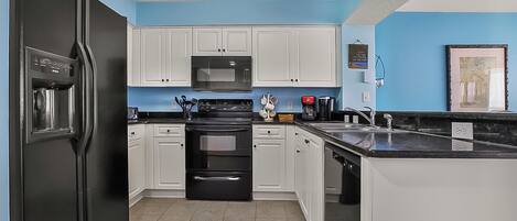 A compact kitchen with white cabinets, a black refrigerator, a microwave, and a stove.