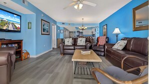 A living room with a brown leather sofa, a wooden coffee table, and a television mounted on the wall. - Crescent Shores 1308 Oceanfront, Pools, Lazy River (North Myrtle Beach)