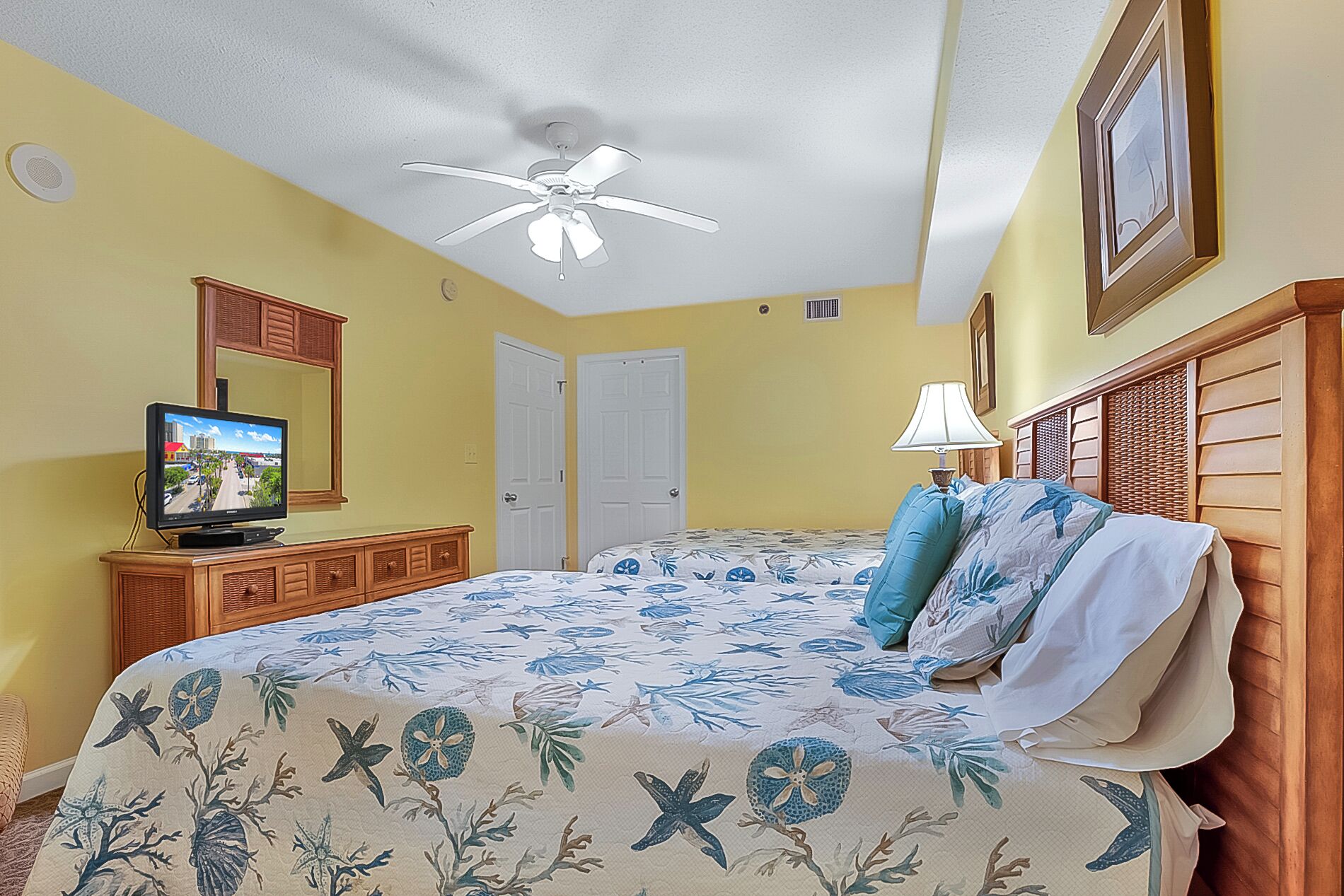 A hotel room with a bed, a television, a ceiling fan, and a door.