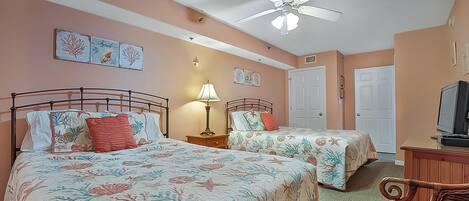 A bedroom with two beds, a ceiling fan, a desk with a computer, and artwork on the walls.