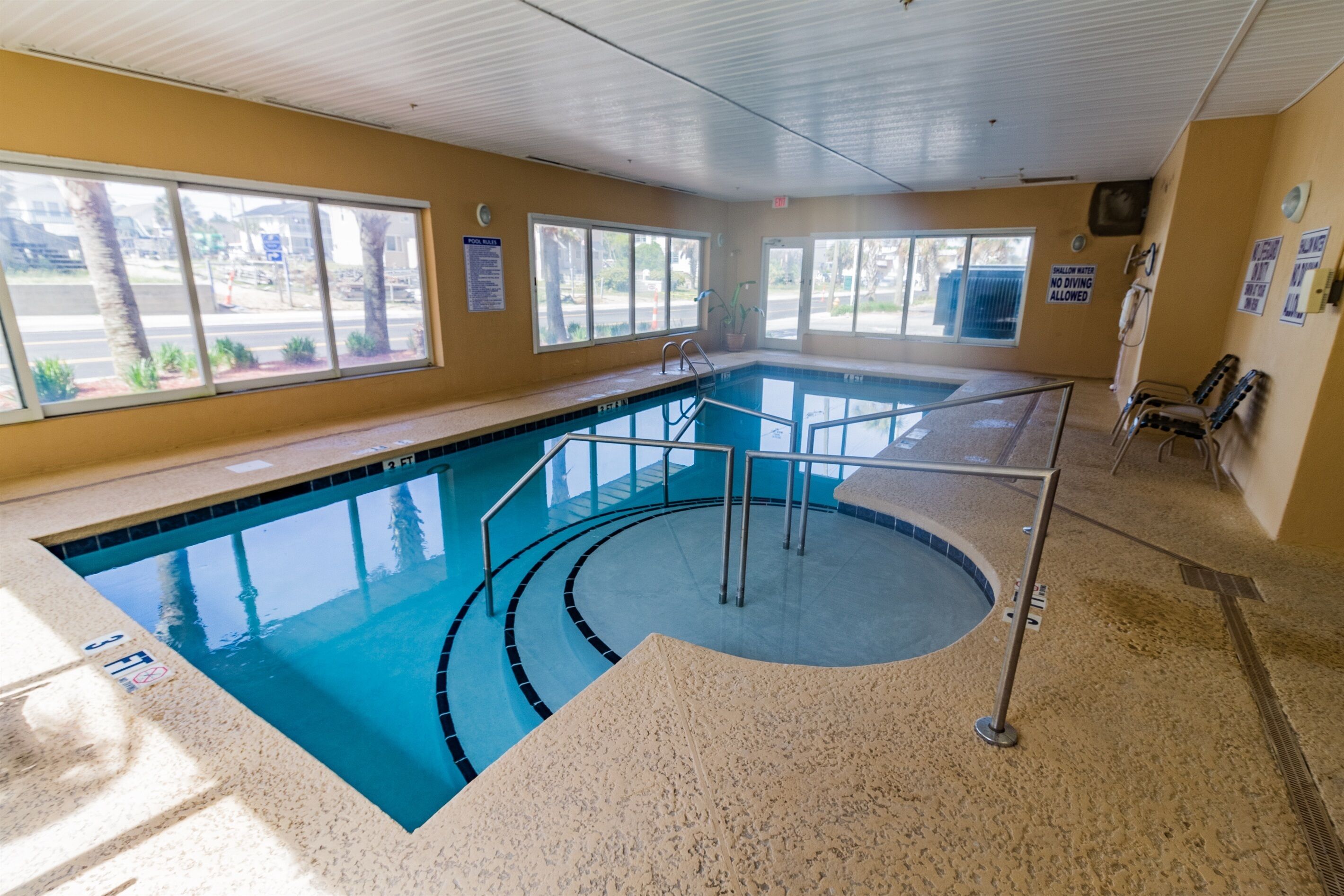 An indoor swimming pool with clear water, a tiled floor, and a pool ladder.