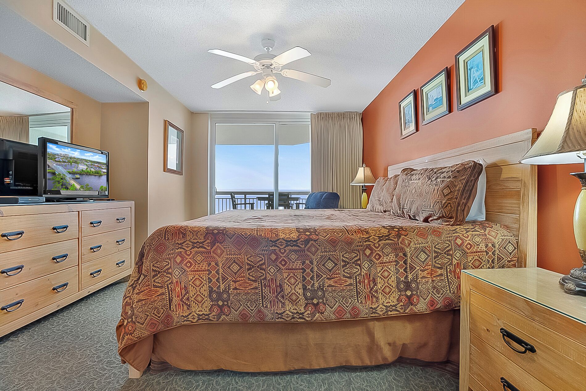 Een hotelkamer met een groot bed, een plafondventilator, een televisie op een dressoir en een balkon met uitzicht.