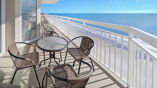 A balcony with wicker chairs and a glass table, overlooking a beach with a clear view of the ocean. - Crescent Shores 1601 Oceanfront, Pools,Lazy River (North Myrtle Beach)