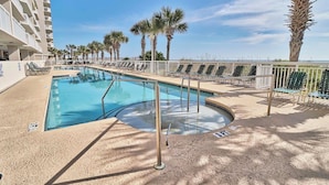 A swimming pool with sun loungers and palm trees, surrounded by a white fence and a building with balconies. - Crescent Shores 1601 Oceanfront, Pools,Lazy River (North Myrtle Beach)