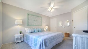 A bedroom with a bed, a ceiling fan, a nightstand, a lamp, a wall decoration, and a door with mirrors. - Raised Beach Cottage #62, 3 Pools, Beach (Myrtle Beach)