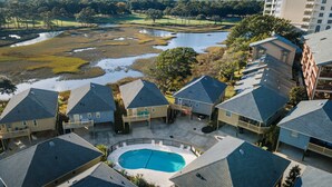 A residential area with houses, a swimming pool, and a view of a natural landscape including a pond and trees. - Raised Beach Cottage #62, 3 Pools, Beach (Myrtle Beach)