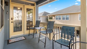 A covered porch with a sliding glass door, outdoor seating with metal chairs, and a view of neighboring houses. - Raised Beach Cottage #62, 3 Pools, Beach (Myrtle Beach)
