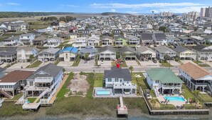 Una zona residencial costera con casas que tienen balcones, una piscina y un muelle que se adentra en el agua.