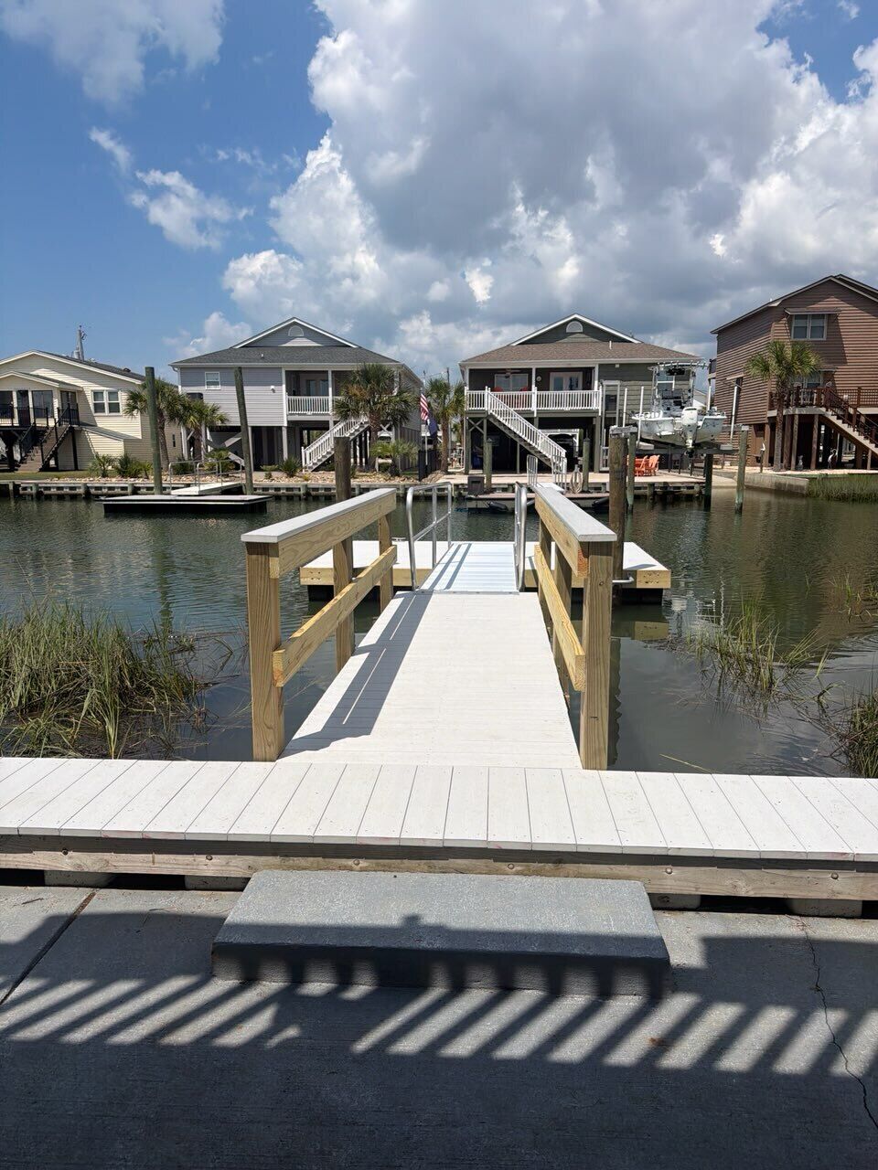 A wooden dock leading to a marina with houses in the background.