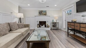 Una sala de estar con chimenea blanca, un sofá, una mesa de centro y un televisor montado en la pared.