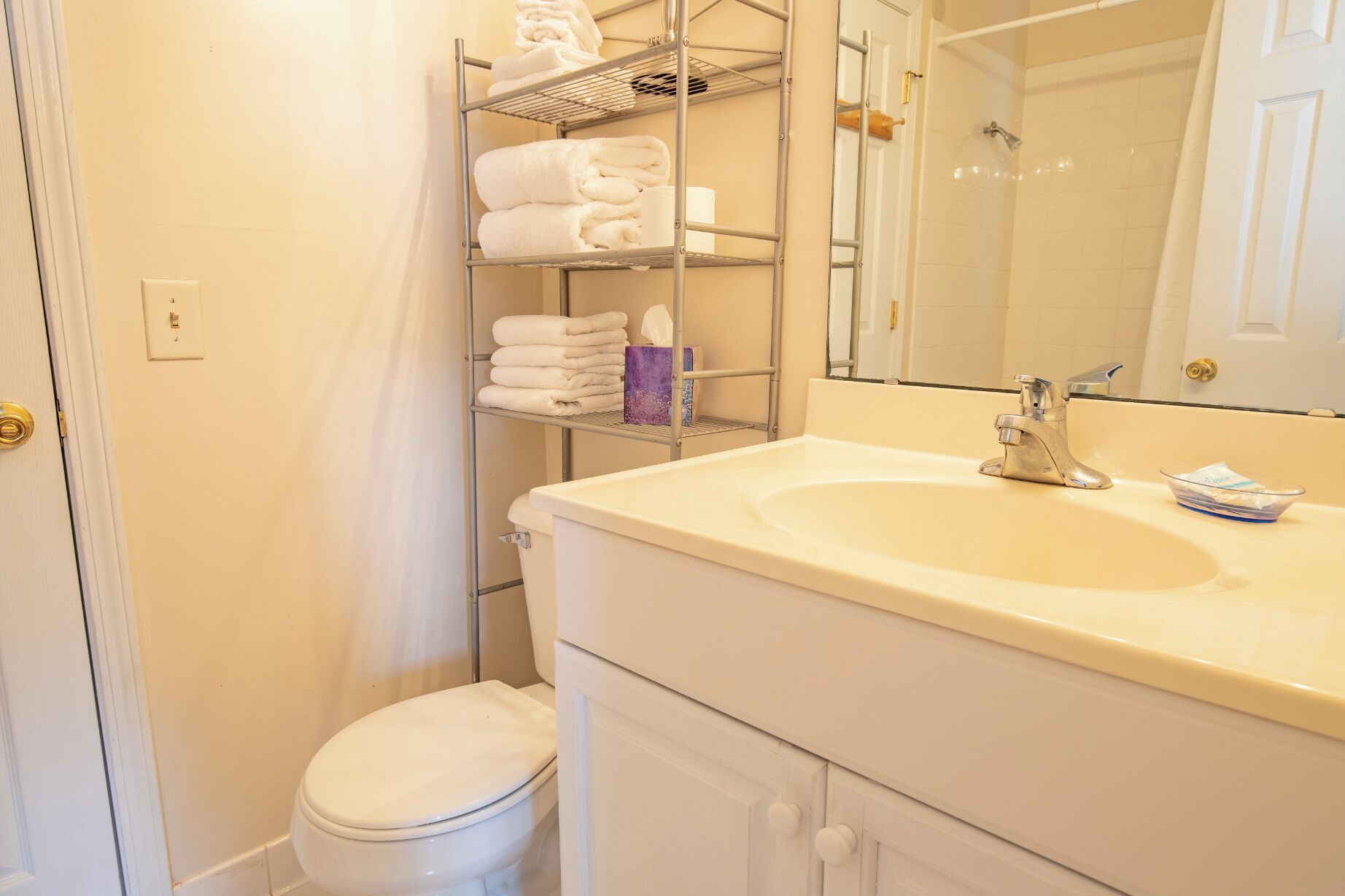A bathroom with a toilet, a sink with a mirror, and a towel rack with folded towels.