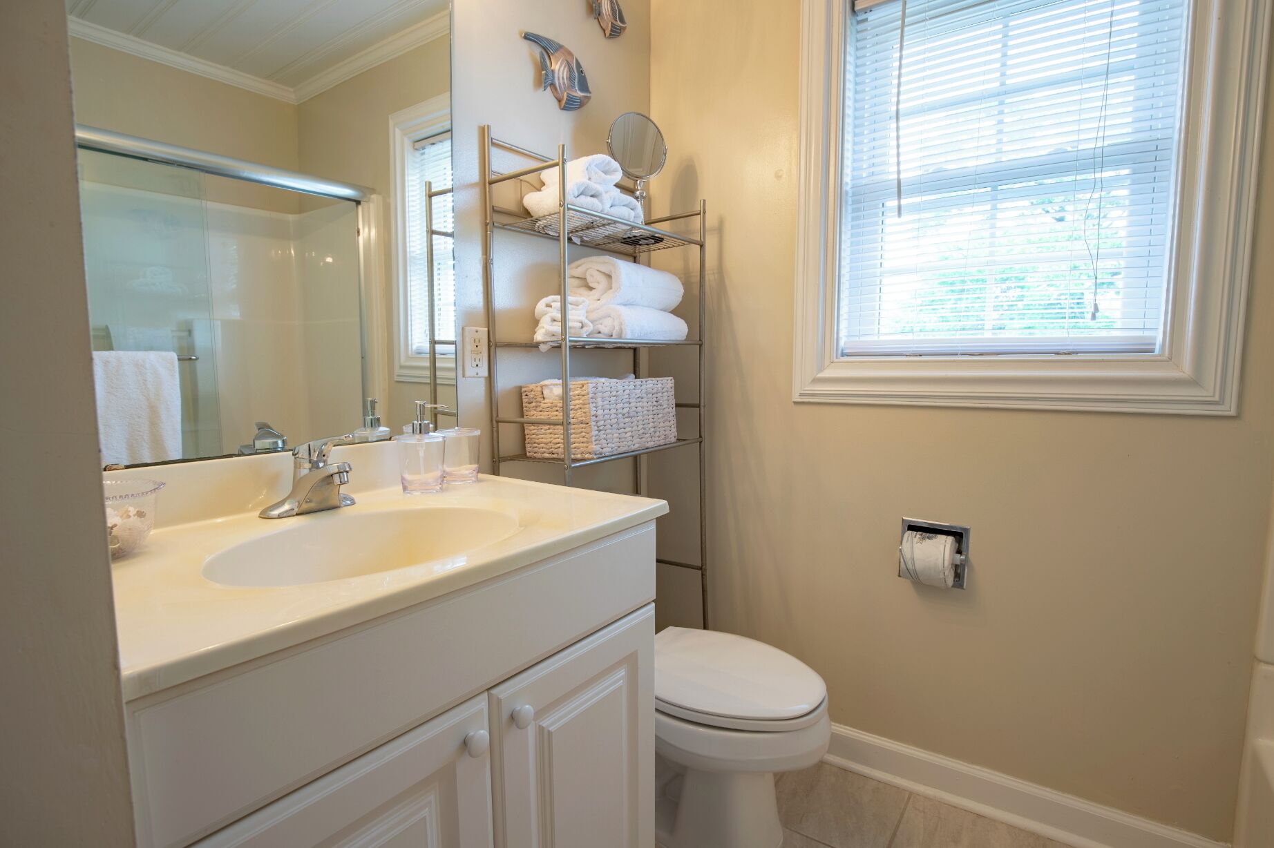 A bathroom with a white sink, mirror, and toilet. There is a towel rack with towels and a basket.