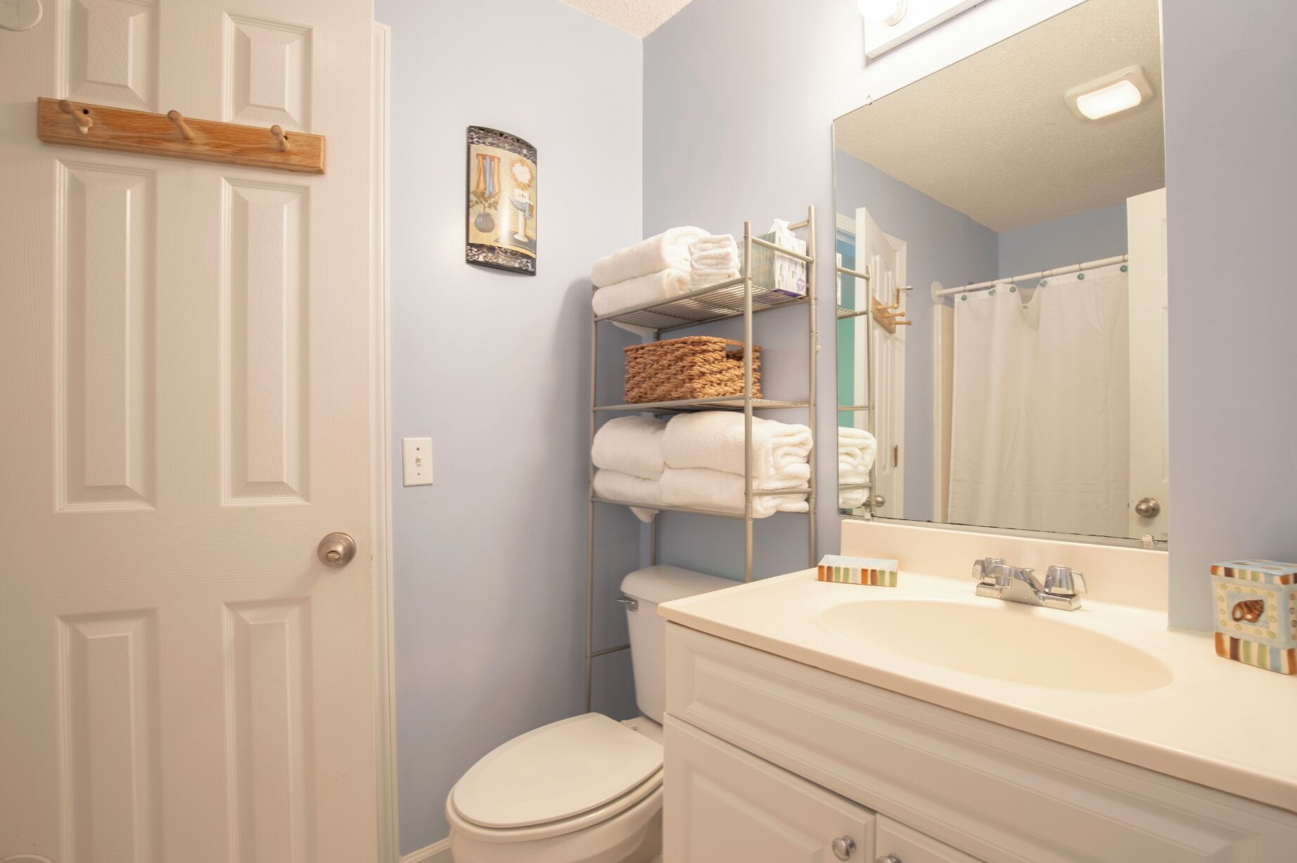 Une salle de bain avec des toilettes blanches, un lavabo avec un miroir et des étagères contenant des serviettes et des paniers.